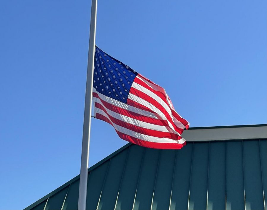 An American flag is flown at half mast in front of a cloudless autumn  sky.