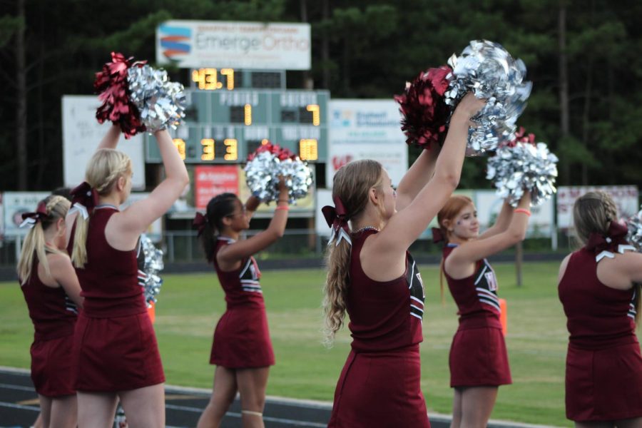 The cheerleaders raise their pom-poms high during an intense football game.