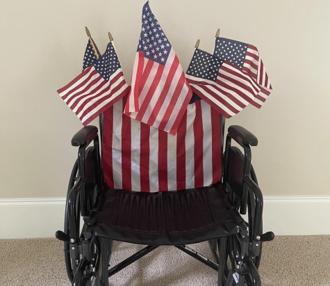 A wheelchair sits adorned with American flags in a beige room.