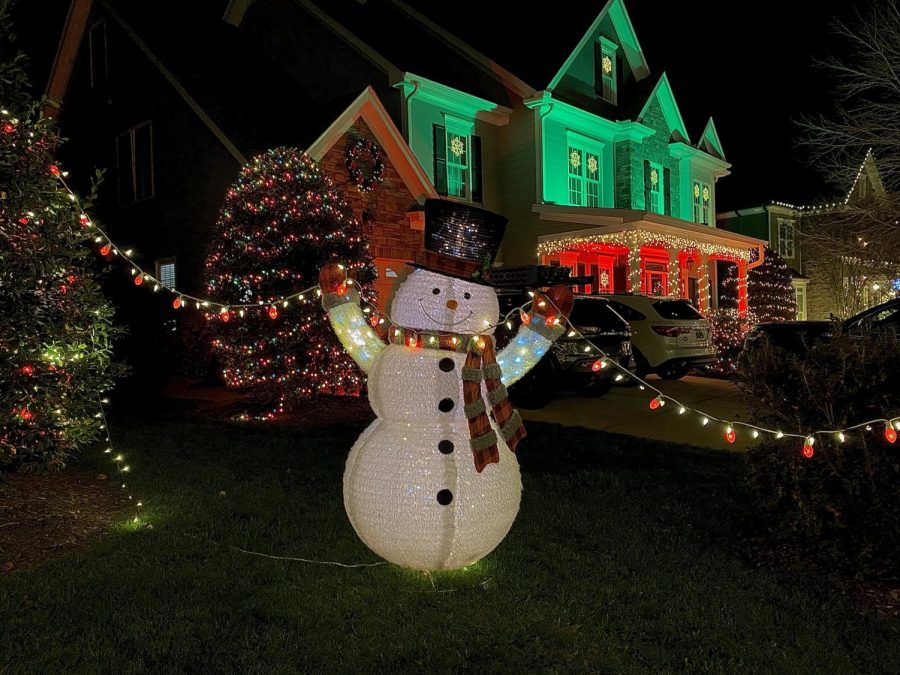 A large snowman holds up two strands of lights to greet walkers in the neighborhood.